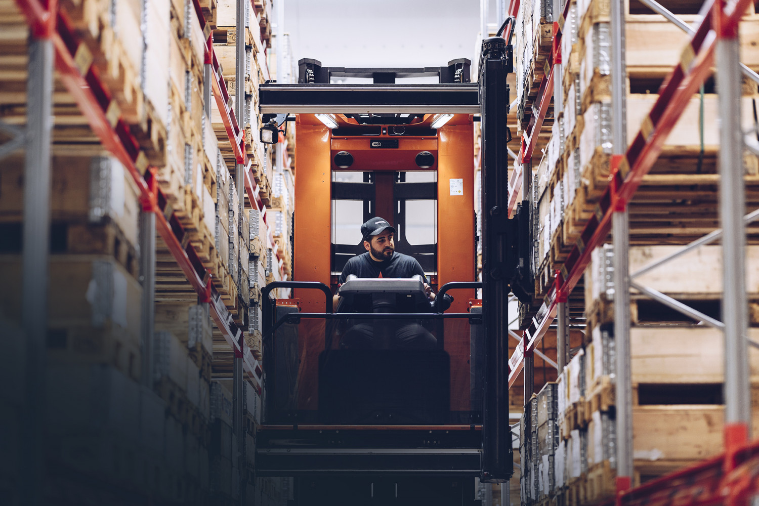 Large orange electric forklift truck in a warehouse, steered by a man with a cap
