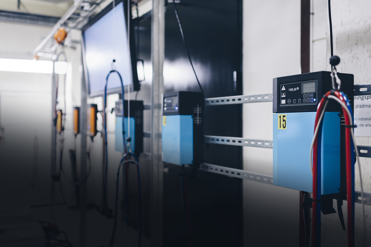 A lithium ion industrial battery charging system, mounted on the wall with a computer screen in the background.