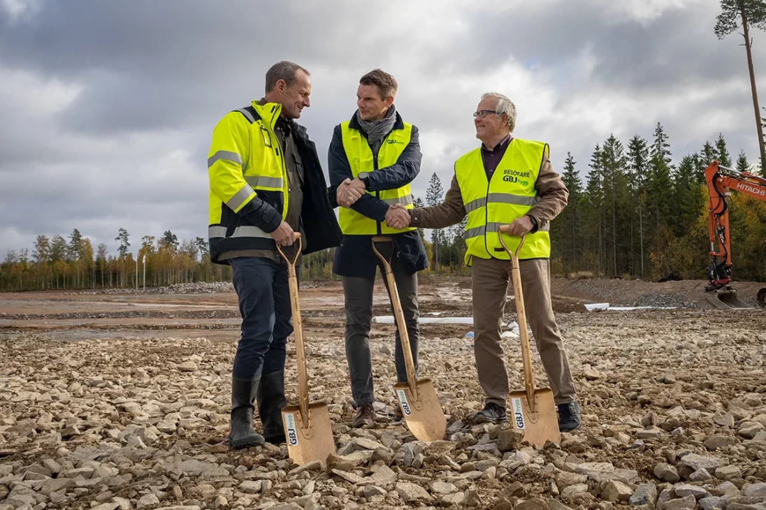 Tre män med gula västar och spadar skakar hand